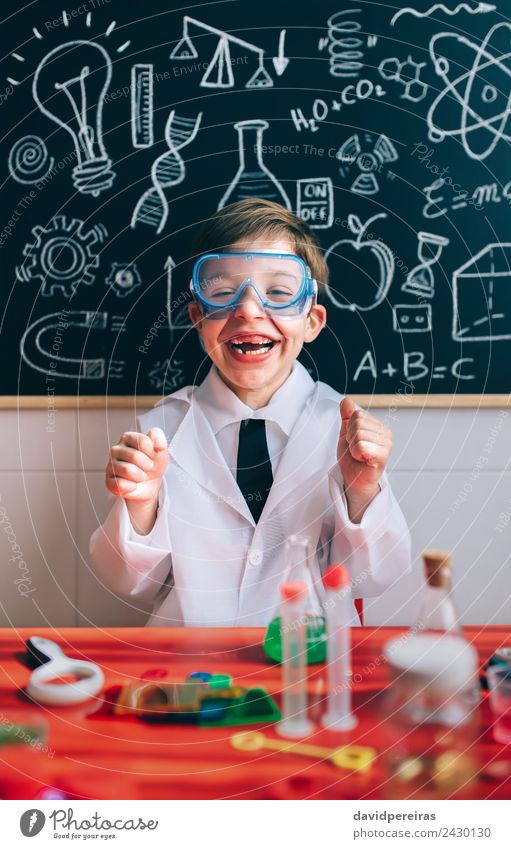 Kleiner Wissenschaftler lachend hinter dem Tisch mit den Experimentierelementen Flasche Glück Spielen Wohnung Wissenschaften Kind Schule Klassenraum Tafel Labor