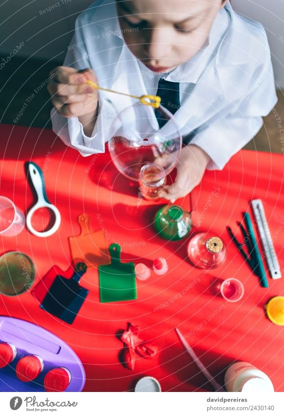 Kind macht Seifenblasen über dem roten Tisch. Flasche Freude Glück Spielen Wohnung Wissenschaften Schule Klassenraum Labor Mensch Junge Kindheit Hand
