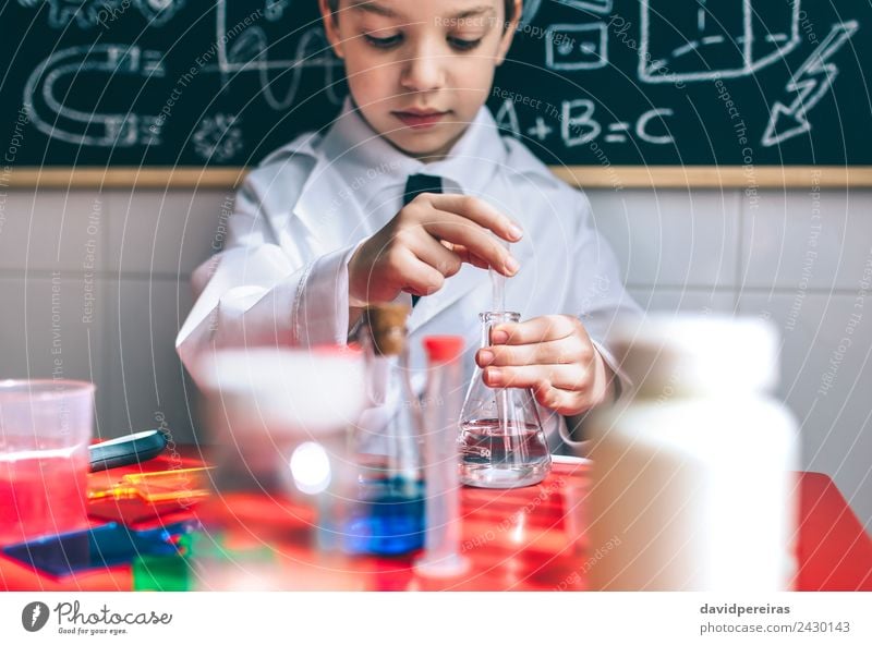 Ernsthaftes Kind beim Spielen mit chemischen Flüssigkeiten Flasche Glück Wohnung Tisch Wissenschaften Klassenraum Tafel Labor Mensch Junge Kindheit Hand