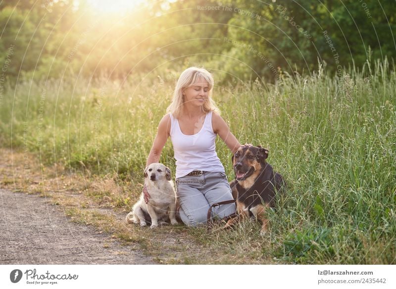 Blonde Frau mit ihren beiden Hunden auf dem Land Glück Gesicht Sommer Erwachsene Freundschaft 1 Mensch 45-60 Jahre Tier Wärme Gras Wiese blond Haustier Lächeln