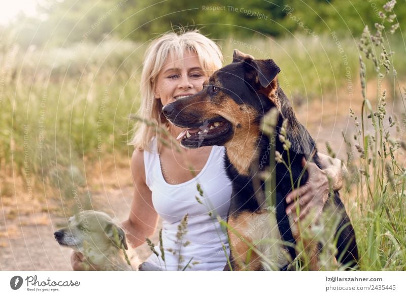 Hübsche blonde Frau mit ihren beiden Hunden. Glück Gesicht Sommer Erwachsene Freundschaft 1 Mensch 45-60 Jahre Tier Wärme Gras Wiese Haustier Lächeln Liebe