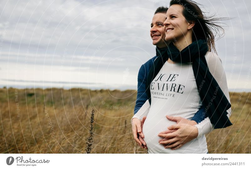 Schwangerschaft mit Partnerumarmung und Bauchhaltung Lifestyle Glück schön Mensch Frau Erwachsene Mann Mutter Paar Landschaft Wind Gras Wiese Schal berühren
