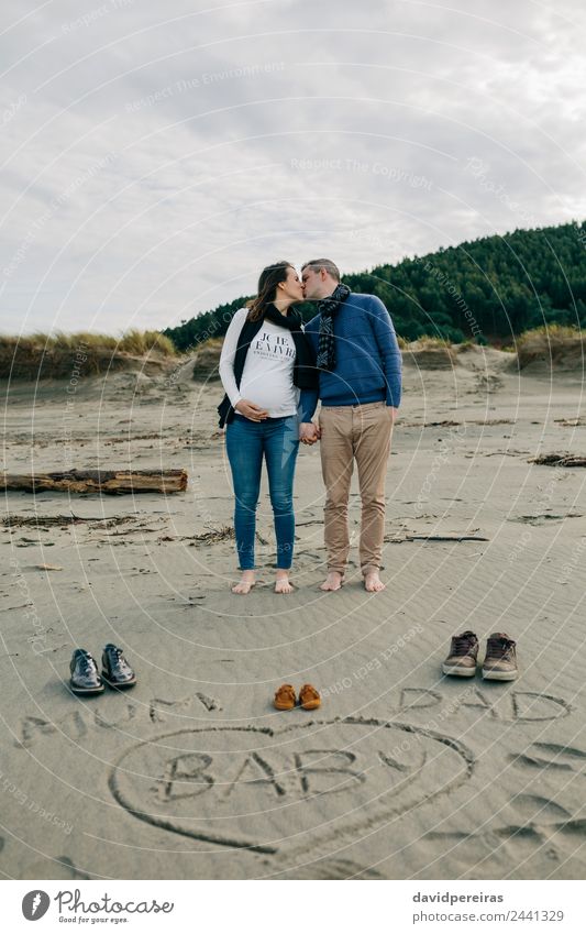 Mama, Papa und Baby auf den Sand geschrieben, wobei die Eltern sich küssen. Lifestyle Strand Winter Mensch Frau Erwachsene Mann Mutter Vater