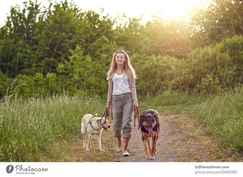 Fröhliche junge Frau geht mit ihren Hunden spazieren. Lifestyle Glück schön Sommer Erwachsene Freundschaft 1 Mensch 18-30 Jahre Jugendliche Natur Tier Wärme