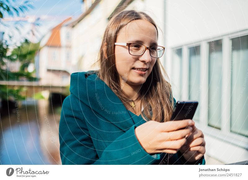 junge Frau mit blauem Mantel steht am Fluss und tippt in Smartphone Lifestyle Stil Freude Glück Mensch feminin Junge Frau Jugendliche Leben Lebensfreude