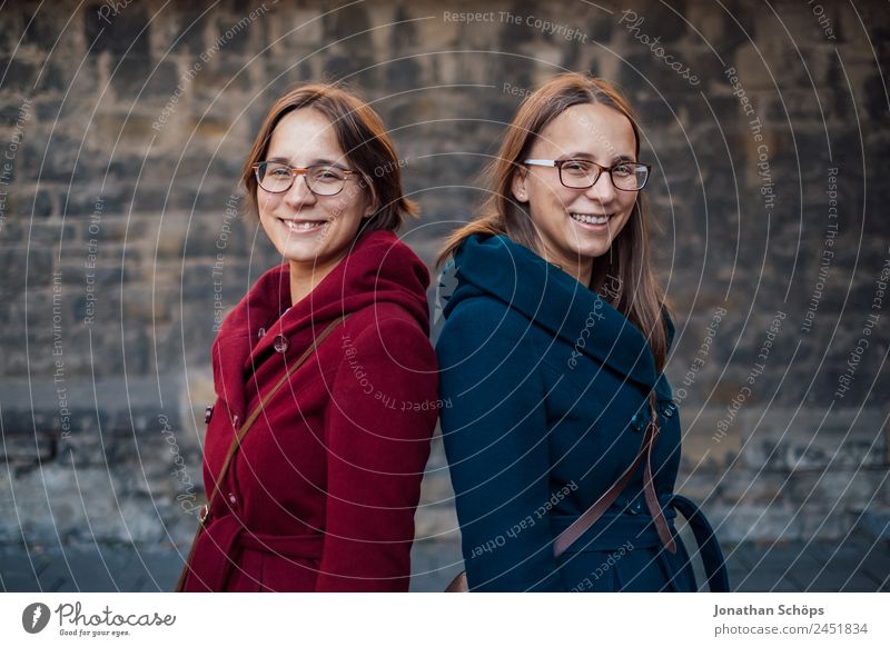 Zwillingsschwestern stehen lachend Rücken an Rücken vor Steinmauer Lifestyle Stil Freude Glück Mensch feminin Junge Frau Jugendliche Geschwister Schwester Leben