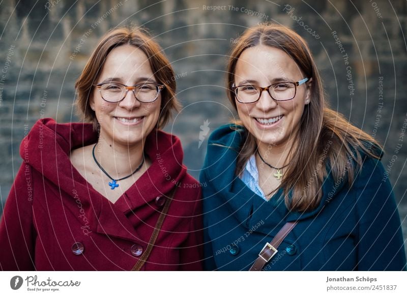 lachende Zwillingsschwestern vor Mauer mit rotem und blauen grünem Mantel Lifestyle Stil Freude Glück Mensch feminin Junge Frau Jugendliche Geschwister