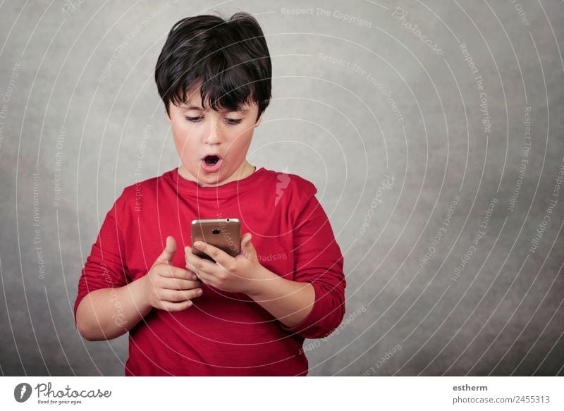 überraschtes Kind mit einem Mobiltelefon auf grauem Hintergrund Lifestyle Spielen Telefon Funktelefon Bildschirm Technik & Technologie Unterhaltungselektronik