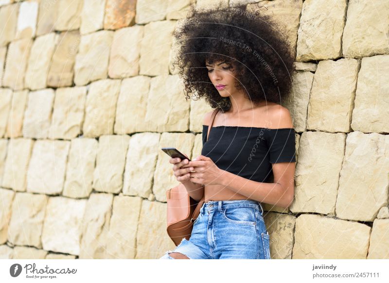 Ernste schwarze Frau mit Afro-Haar schaut auf ihr Smartphone im Freien. Lifestyle Stil schön Haare & Frisuren Telefon PDA Technik & Technologie Mensch