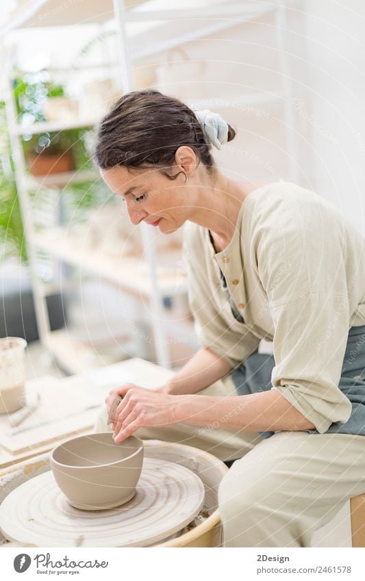 Junge Frau sitzt am Tisch und stellt Ton- oder Keramikbecher her. Geschirr Freizeit & Hobby Handarbeit Arbeit & Erwerbstätigkeit Beruf Handwerker Arbeitsplatz