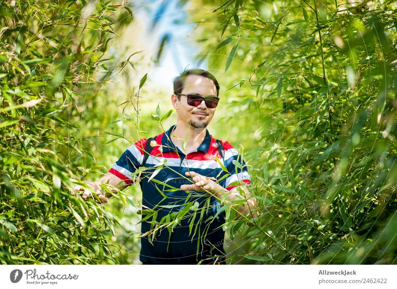 Portrait von einem jungen Mann im Bambus Dschungel Porträt Junger Mann 1 Mensch Sonnenbrille grün Natur Tag Sträucher Blatt Wald Urwald Ferien & Urlaub & Reisen