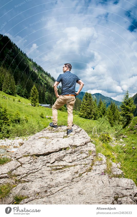junger Mann posiert auf Fels vor Bergpanorama Tag Schönes Wetter Wolken Natur grün Baum Wald Berge u. Gebirge Idylle Ferien & Urlaub & Reisen Reisefotografie