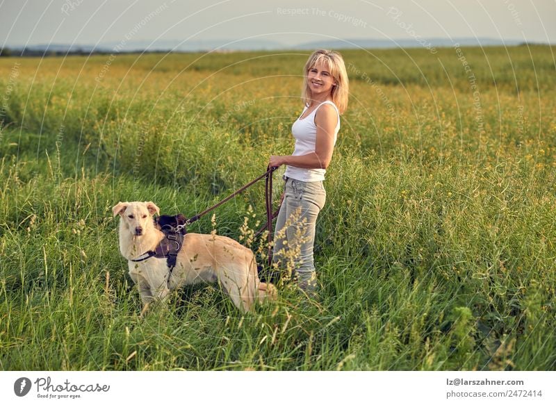 Blonde Frau geht bei Sonnenuntergang mit ihren Hunden spazieren. Lifestyle schön Sommer Erwachsene Freundschaft 1 Mensch 45-60 Jahre Natur Landschaft Tier Wärme