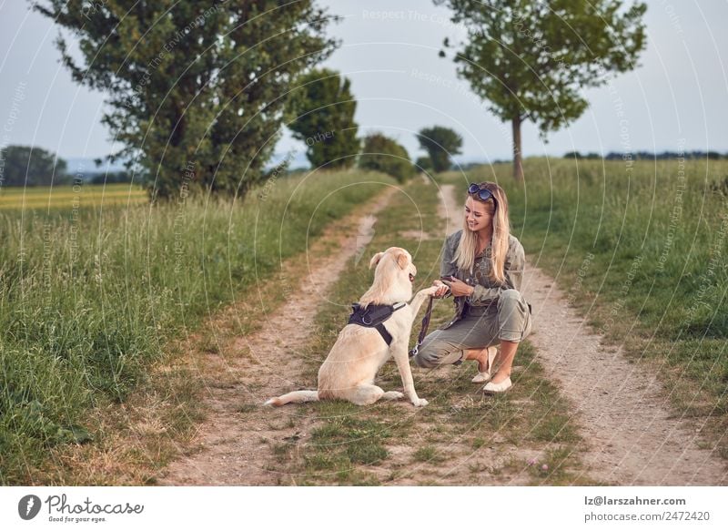Liebevolle junge Frau bot eine Pfote von ihrem Hund an. Sommer Erwachsene Freundschaft Landschaft Tier Wege & Pfade blond gold Labrador ländlich Textfreiraum