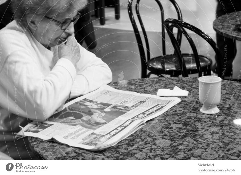 Oma im Bistro Großmutter Senior Zeitung lesen Straßencafé Bar Restaurant trinken Getränk Frau Weiblicher Senior Einsamkeit Schwarzweißfoto Ovomaltine Schoggi