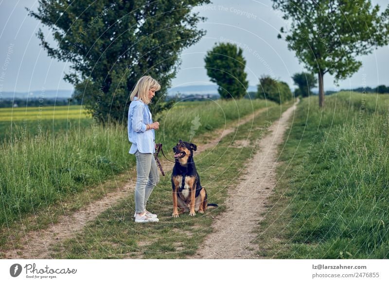 Attraktive junge Frau, die ihren Hund unterrichtet. Sommer Erwachsene Freundschaft 1 Mensch 45-60 Jahre Landschaft Tier Wege & Pfade blond stehen Lehre ländlich