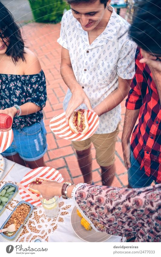 Junger Mann hält Hot Dog in einem Barbecue mit Freunden. Wurstwaren Brot Brötchen Mittagessen Fastfood Limonade Teller Lifestyle Freude Glück Sommer Frau