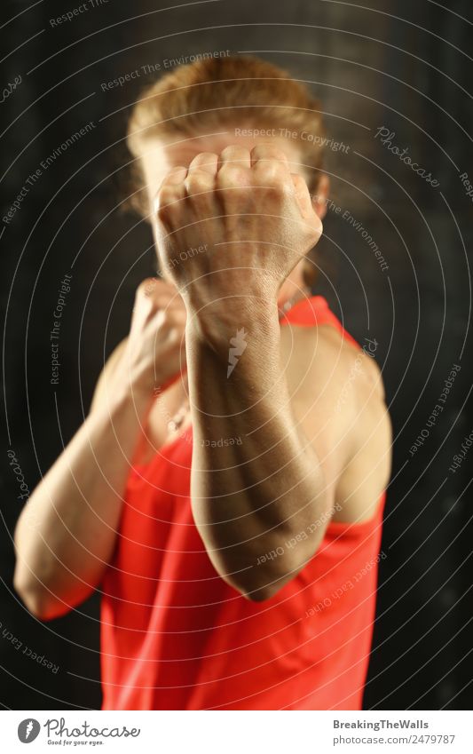 Nahaufnahme Frontalporträt einer jungen sportlichen Frau mittleren Alters in Sportkleidung im Fitnessstudio vor dunklem Hintergrund, stehend in Boxhaltung mit Händen und Fäusten, in die Kamera blickend