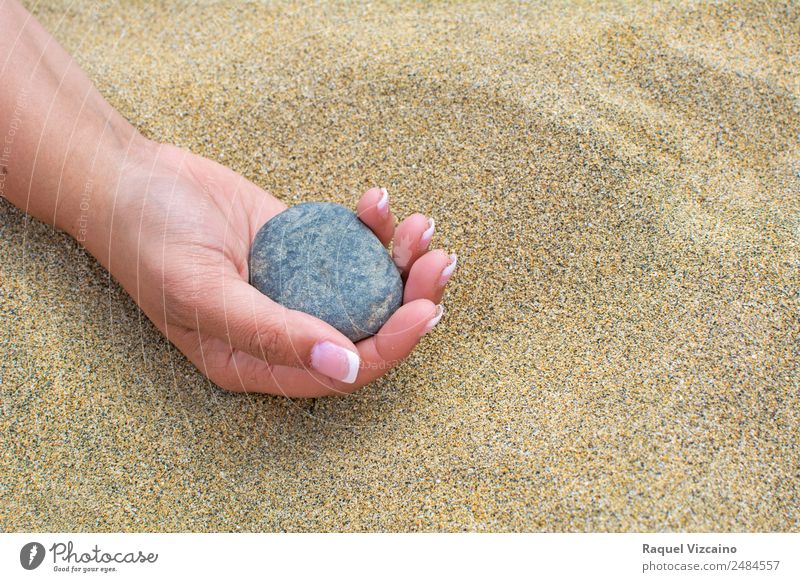 Schöne Hand, die einen Stein hält, auf einem Sandhintergrund am Strand. Lifestyle Sommer Sommerurlaub feminin Sonne Schönes Wetter genießen leuchten Gesundheit