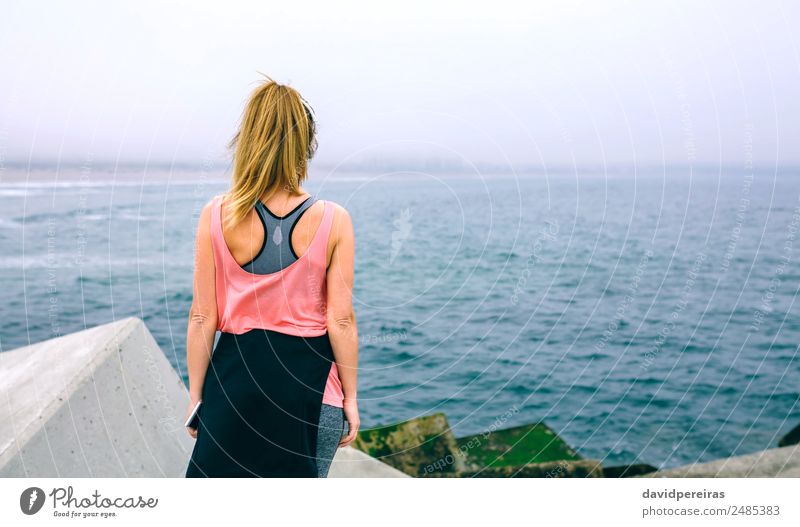 Nicht erkennbare junge Frau, die das Meer beobachtet. Lifestyle Wellness Erholung ruhig Sport Telefon PDA Mensch Erwachsene Nebel Beton beobachten Fitness