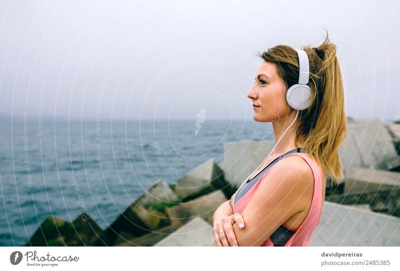 Sportlerin mit Kopfhörern, die das Meer beobachtet. Lifestyle Wellness Erholung ruhig Musik Mensch Frau Erwachsene Nebel Beton beobachten Denken Fitness hören