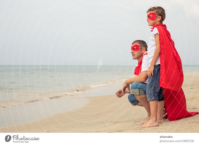 Vater und Sohn spielen tagsüber am Strand Superhelden. Die Leute haben Spaß im Freien. Konzept des Sommerurlaubs und der freundlichen Familie. Lifestyle Freude