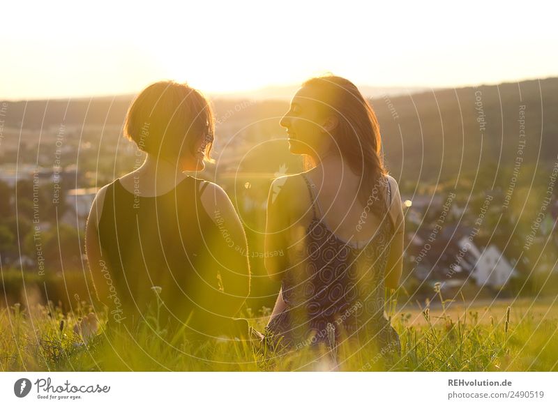 Schwestern sitzen auf einer Wiese im Sonnenuntergang Frau Liebe Glück Zusammensein Sommer Lebensfreude Erholung Freundschaft Zusammenhalt Rückansicht Unschärfe
