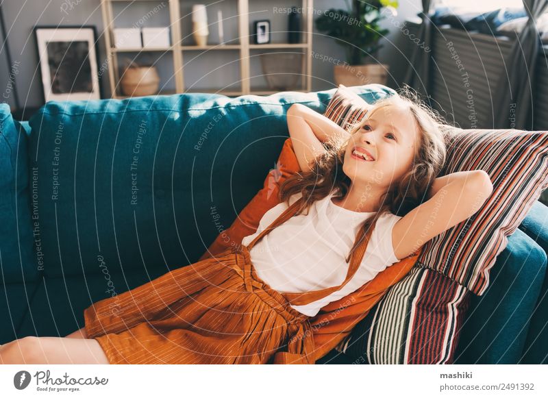fröhliches Kind Mädchen, das sich auf der gemütlichen Couch im modernen Wohnzimmer entspannt. Lifestyle Glück Wohnung Haus Umzug (Wohnungswechsel)