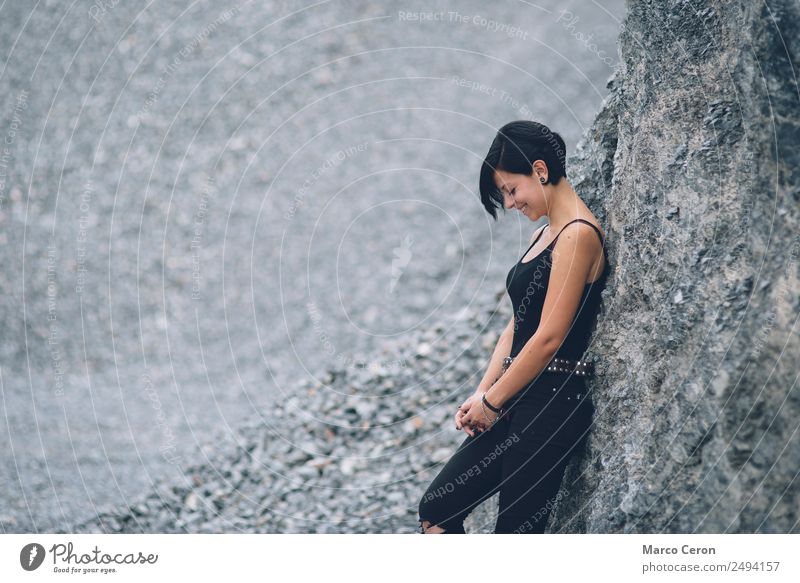 schönes brünettes kurzhaariges Mädchen, das sich an eine graue Felswand lehnt und draußen glücklich lächelt attraktiv Hintergrund schwarz Atmung Kaukasier Tag