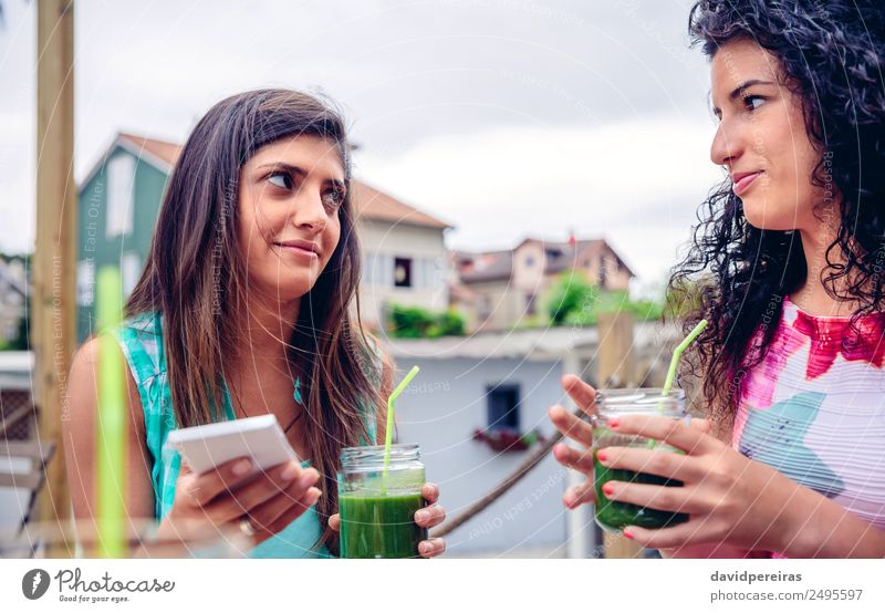 Zwei Frauen schauen sich an und halten grüne Smoothies in der Hand. Gemüse Frucht Ernährung Diät Getränk Saft Lifestyle Glück Sommer Telefon PDA