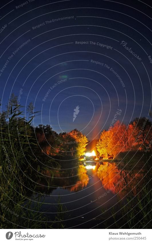 "Oben fährt der große Wagen". Das Oktoberfeuer spiegelt sich im stillen Wasser eines See's im Vordergrund. Am Himmel ist der Große Wagen zu erkennen.