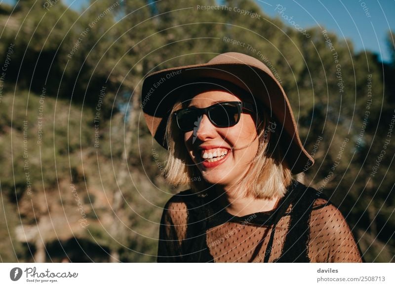 Porträt einer blonden Frau mit Hut und Sonnenbrille, die sich bei Sonnenuntergang in der Natur vergnügt. Lifestyle Stil Freude schön Wellness Leben Wohlgefühl