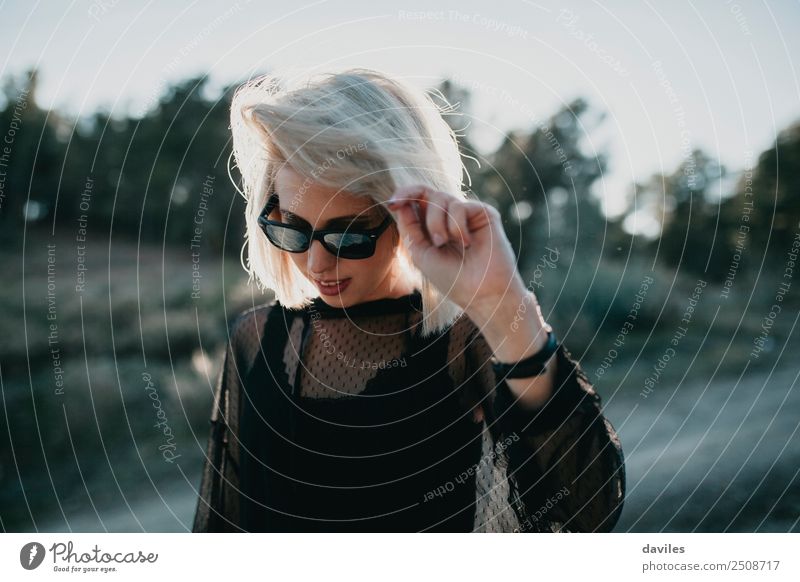 Blondes Mädchen mit Sonnenbrille und schwarzem Kleid, das in der Natur im Gegenlicht geht Lifestyle elegant Stil Freude Ferien & Urlaub & Reisen Ausflug