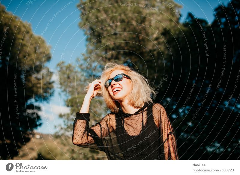 Kühle blonde Frau mit Sonnenbrille und schwarzem Kleid, die sich bei Sonnenuntergang in der Natur amüsiert. Lifestyle elegant Freude Glück schön Wellness Leben