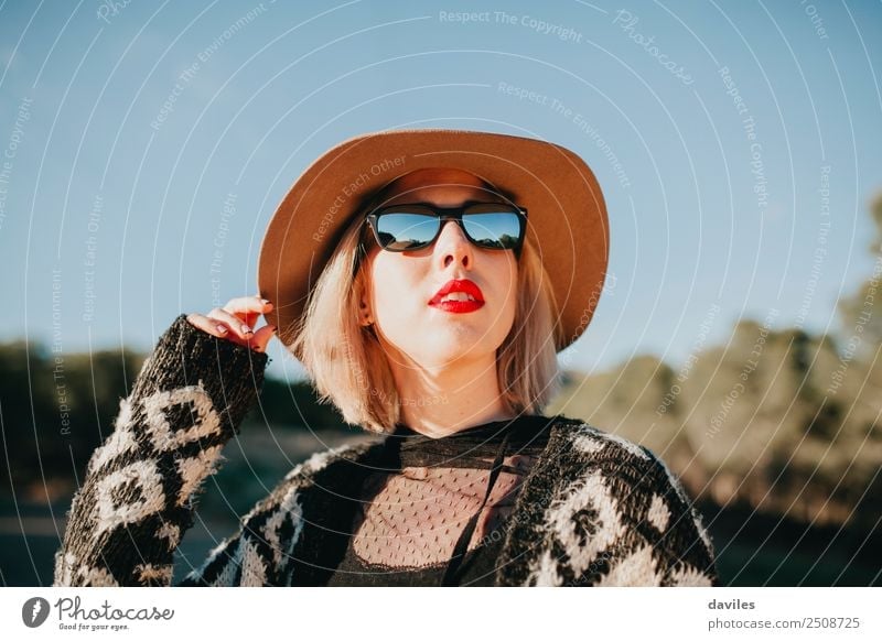 Porträt einer blonden Frau mit Hut, Sonnenbrille und roten Lippen, die bei Sonnenuntergang die Natur genießt. Lifestyle Reichtum elegant Stil schön Mensch