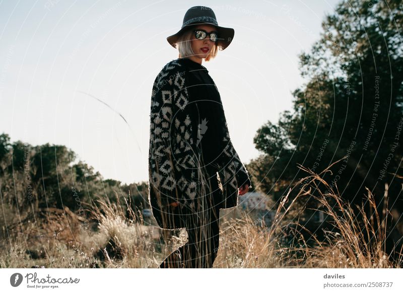 Frau mit Hut und Sonnenbrille, die bei Sonnenuntergang auf einem Feld spazieren geht. Lifestyle Reichtum elegant Stil schön Freizeit & Hobby