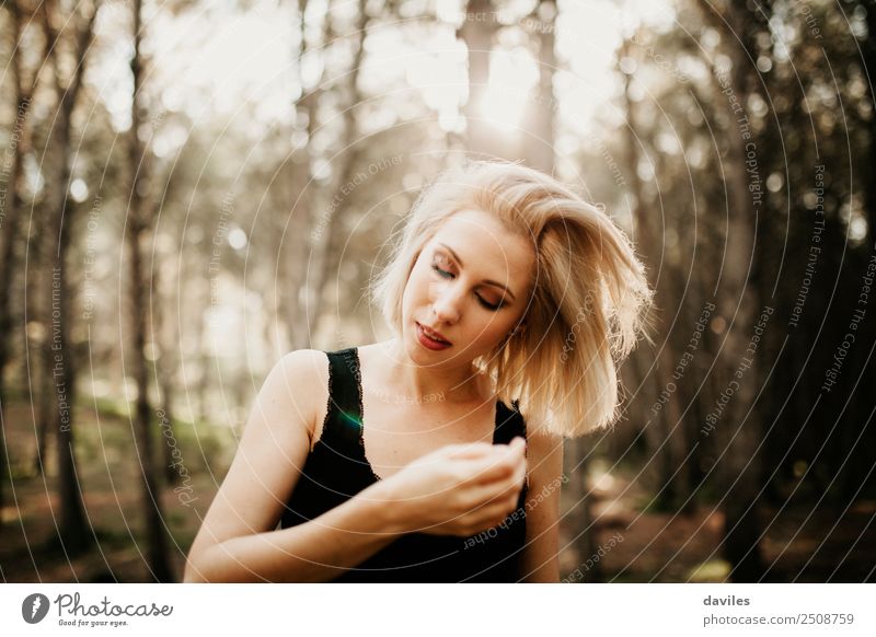 Weiße blonde Frau, die mitten im Wald mit der Sonne im Hintergrund ihr Haar berührt. Lifestyle Stil Haare & Frisuren Wellness Mensch Junge Frau Jugendliche 1