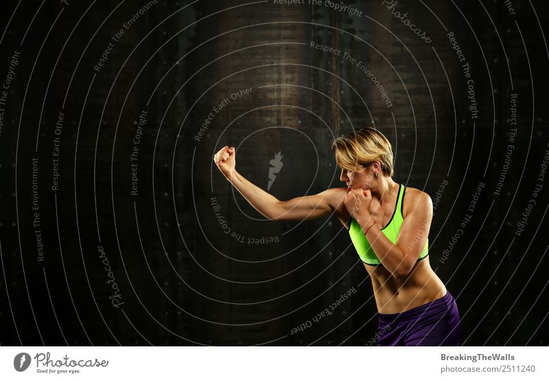 Close up Seitenansicht Profil Porträt einer jungen sportlichen Frau Schattenboxen in Sportkleidung in der Turnhalle über dunklen Hintergrund, wegschauen Fitness