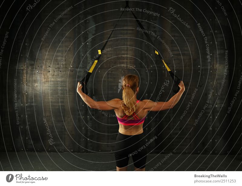 Rückansicht Porträt eines jungen mittleren Alters sportliche Frau beim Crossfit-Training, üben mit trx Aussetzung Fitness-Bänder über dunklen Hintergrund