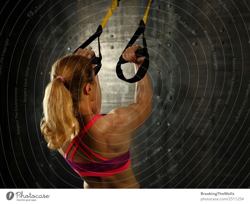 Rückansicht Porträt eines jungen mittleren Alters sportliche Frau beim Crossfit-Training, üben mit trx Aussetzung Fitness-Bänder über dunklen Hintergrund