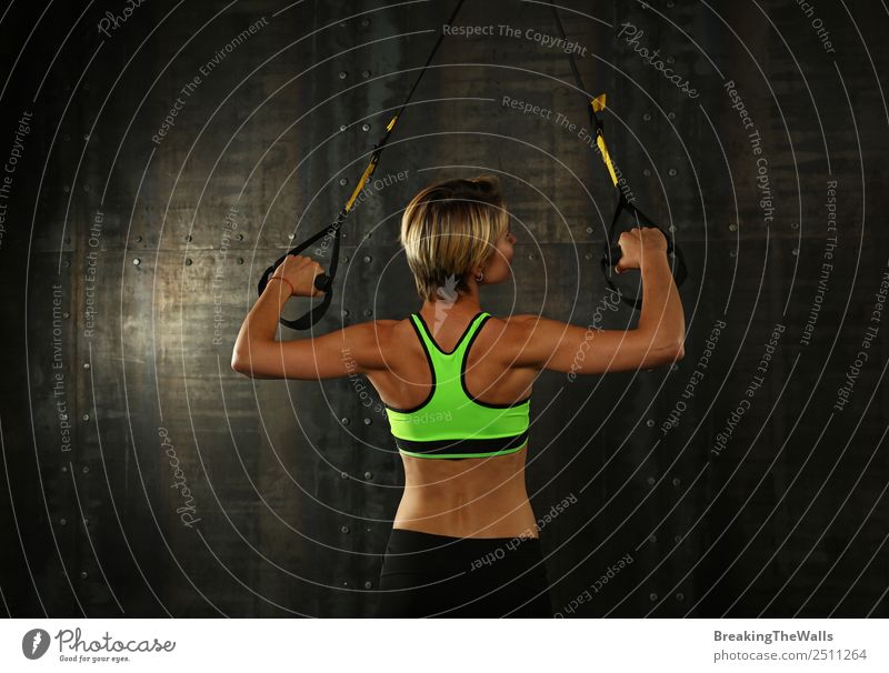 Rückansicht Porträt einer jungen sportlichen Frau beim Crossfit-Training, die mit Trx Suspension Fitness-Bänder über dunklen Hintergrund trainiert Lifestyle