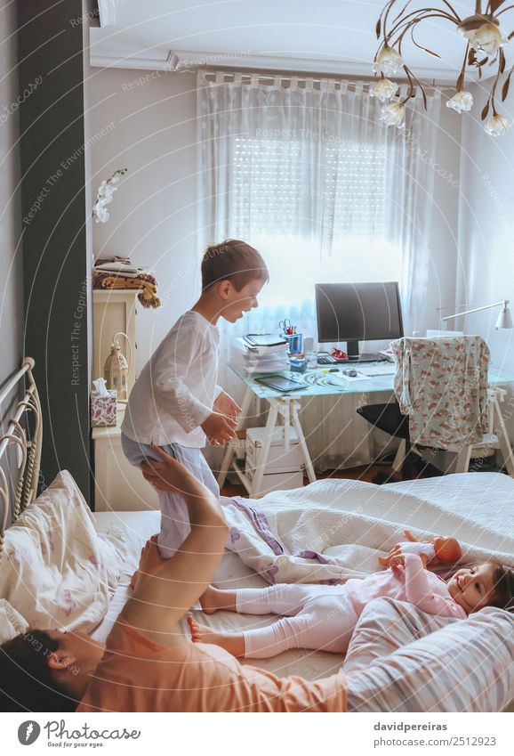 Glücklicher Junge springt und spielt über dem Bett mit seiner Familie an einem entspannten Morgen. Weekend Familie Freizeit Konzept. Lifestyle Freude schön