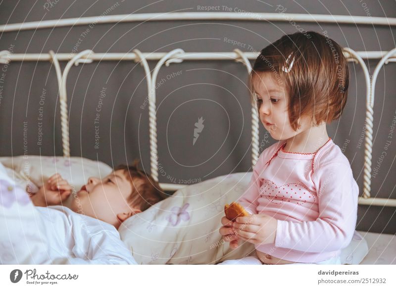 Kleines Mädchen mit Keks, das über dem Bett sitzt. Essen Frühstück Lifestyle Freude Erholung Freizeit & Hobby Schlafzimmer Kind Baby Junge Frau Erwachsene