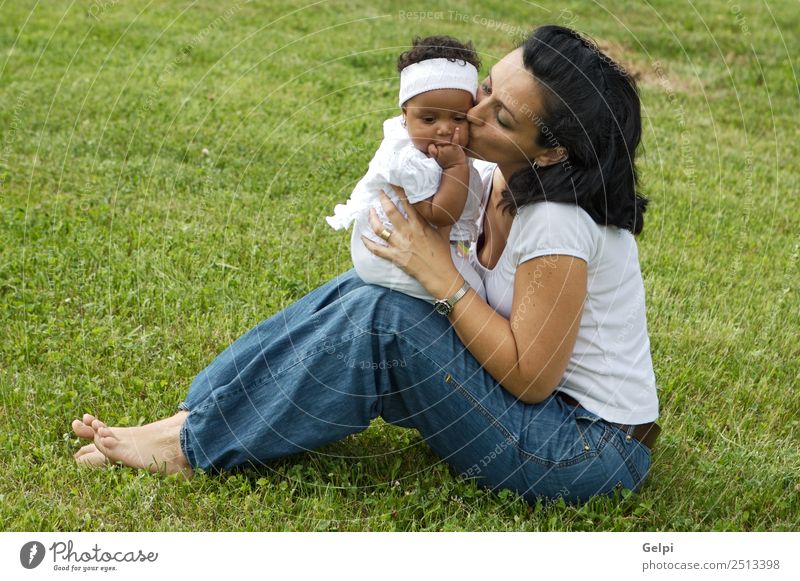 Eine weiße Frau mit einem schwarzen Baby. Glück Leben Mensch Erwachsene Mutter Gras Wiese Küssen Lächeln lachen Fröhlichkeit hell grün Gefühle Farbe Adoption