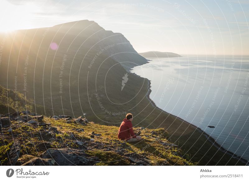 Mensch sitzt an einer Klippe eines Fjordes bei niedrig stehender Sonne am Europäischen Nordmeer Gegenlicht Meer erhaben weite Reflexion & Spiegelung klein Küste