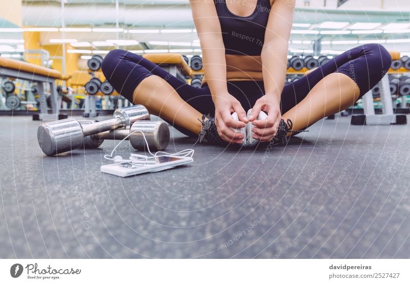 Sportliche Frau sitzt mit Hanteln und Smartphone auf dem Boden des Fitnessstudios. Lifestyle schön Körper Freizeit & Hobby Musik Telefon PDA Mensch Erwachsene