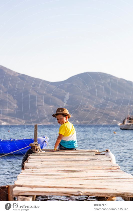 Kleiner Junge auf einem Dock, der auf dem Rücken sitzt und auf den Ozean schaut. Lifestyle Freude Glück Freizeit & Hobby Ferien & Urlaub & Reisen Sommer Strand