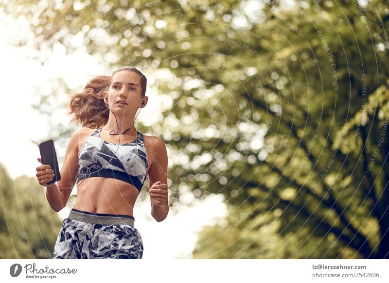 Junge sportliche Frau beim Joggen Lifestyle Sommer Musik Sport PDA Erwachsene 1 Mensch 18-30 Jahre Jugendliche Wärme Park Straße Fitness Lächeln rennen