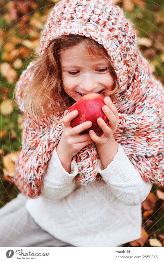 Kind Mädchen isst frischen Apfel im Herbstgarten Frucht Lifestyle Freude Spielen Garten Kindheit Natur Wärme Blatt Wald Schal Lächeln Fröhlichkeit lustig