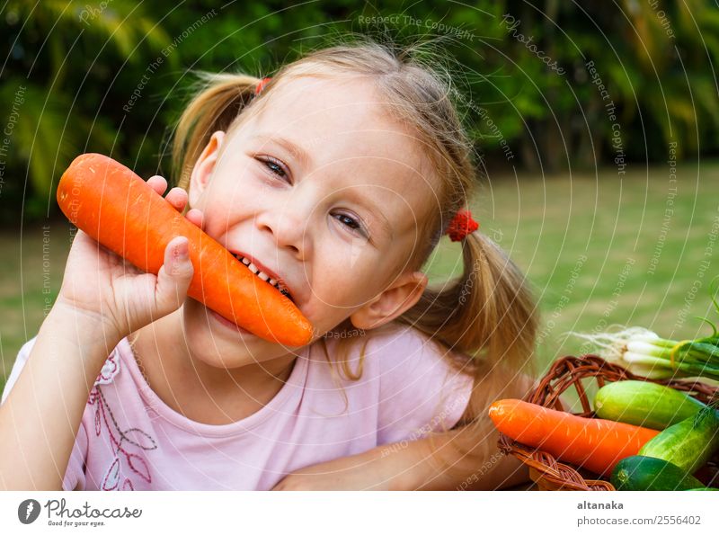 Ein fröhliches kleines Mädchen hält eine Karotte. Gemüse Essen Lifestyle Glück Gesicht Sommer Garten Kind Gartenarbeit Mensch Frau Erwachsene